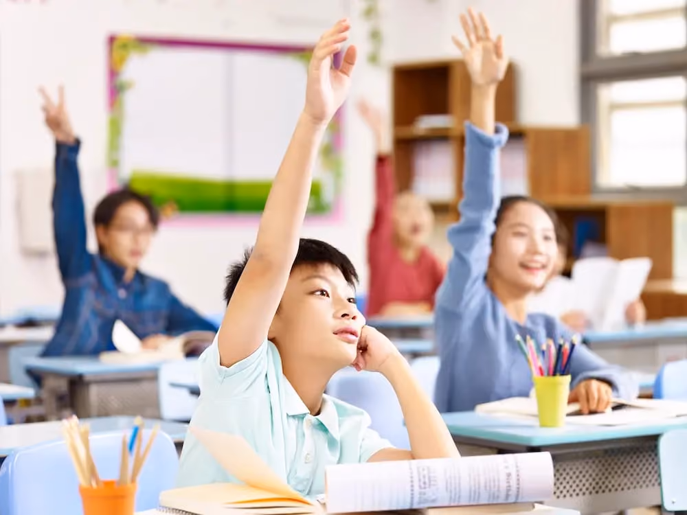 Students in a classroom raising their hands to answer a question.