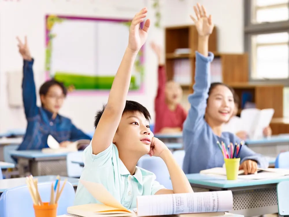 Students in a classroom raising their hands to answer a question.