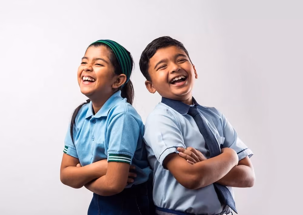 Two schoolchildren in uniforms laughing with arms crossed, standing back to back against a white background.