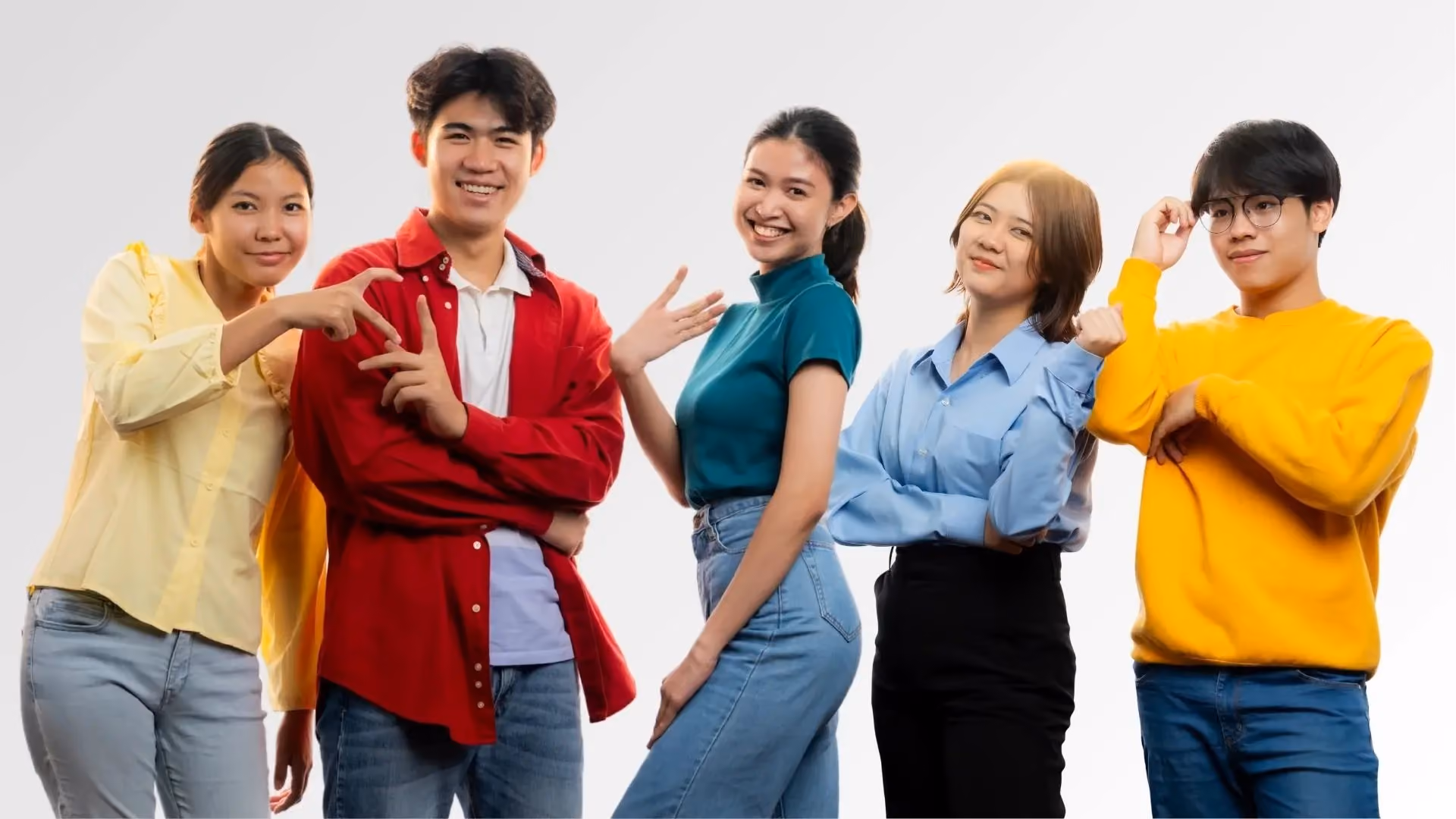 Group of five young adults smiling and posing against white background, wearing casual colorful clothes.