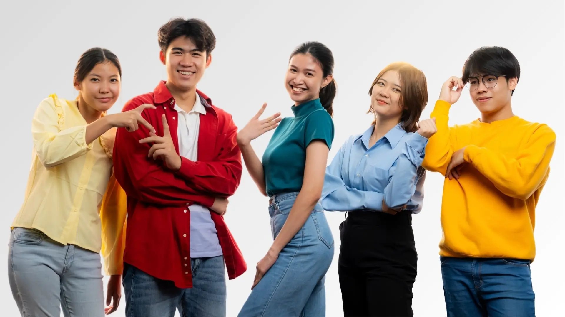 Group of five young adults smiling and posing against white background, wearing casual colorful clothes.