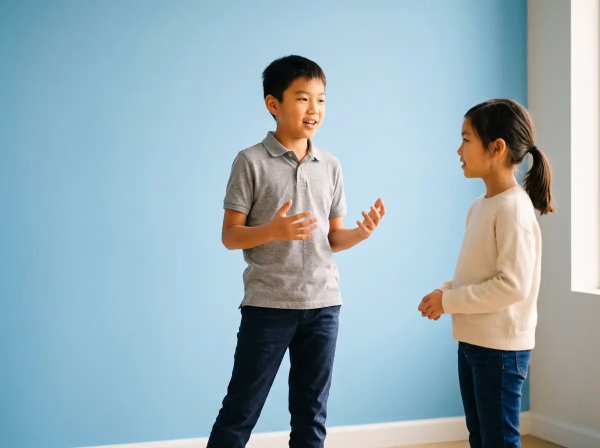 Asian boy in a gray polo shirt speaking confidently to a girl during a pair speaking practice session.
