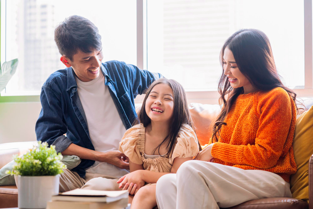 Smiling Asian family of three sitting on couch, enjoying time together in bright living room.