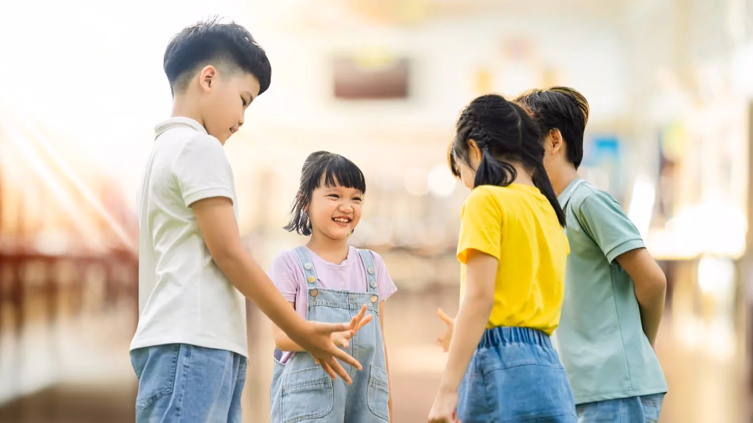 Four children standing in a circle indoors, smiling and interacting with each other.