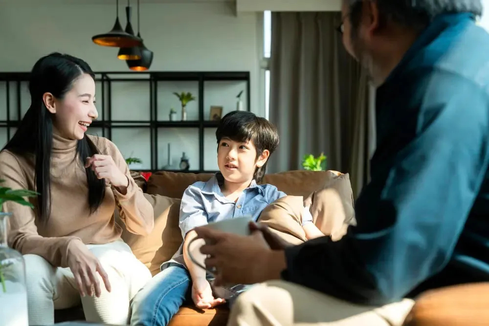 Asian mother and young boy on a sofa talking warmly with grandfather, showing family communication at home.
