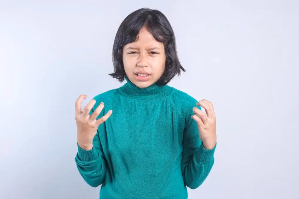 Young child in a green turtleneck with a frustrated expression, illustrating the challenge of public speaking before training.