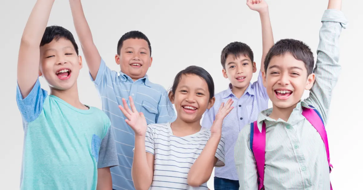 Five happy Asian children smiling and raising their hands in celebration at SuperMinds public speaking classes Singapore.
