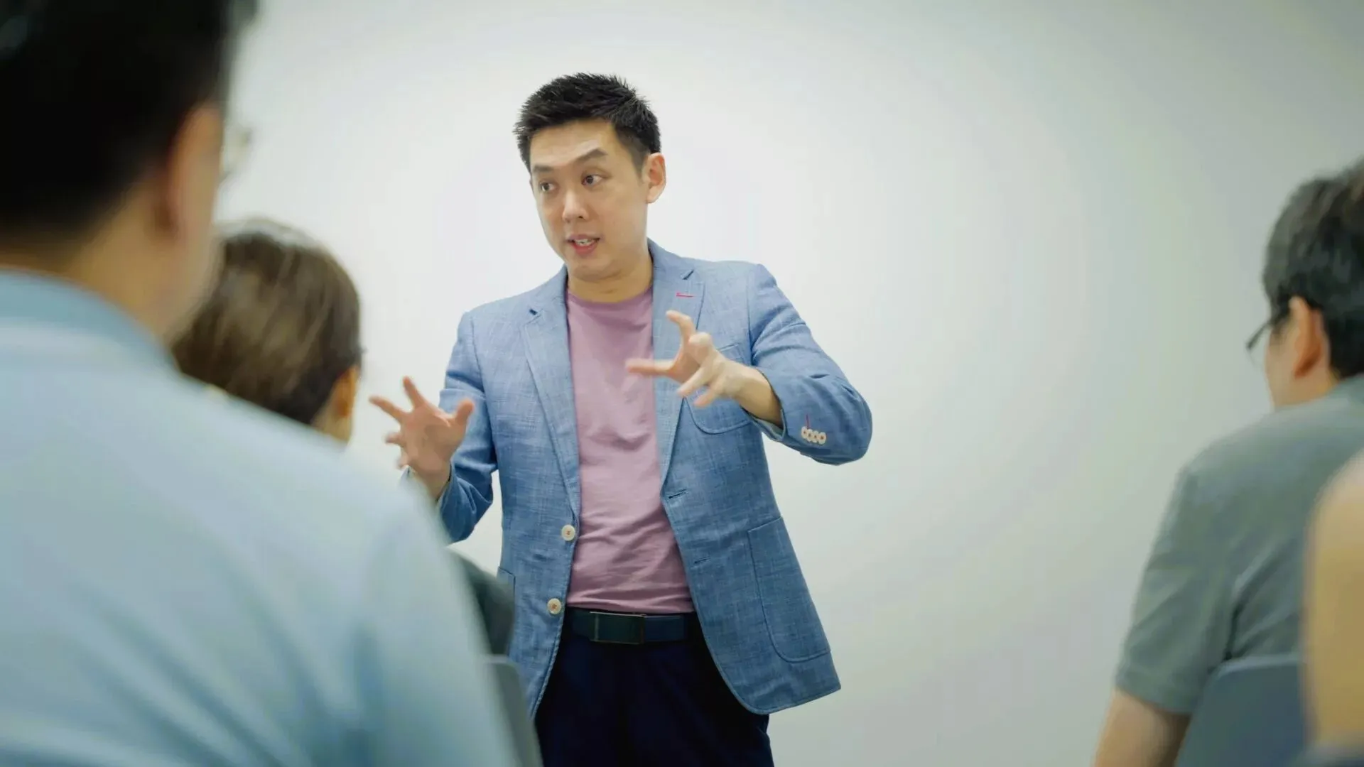 SuperMinds instructor in a blue blazer speaking expressively with hand gestures to a group of students.
