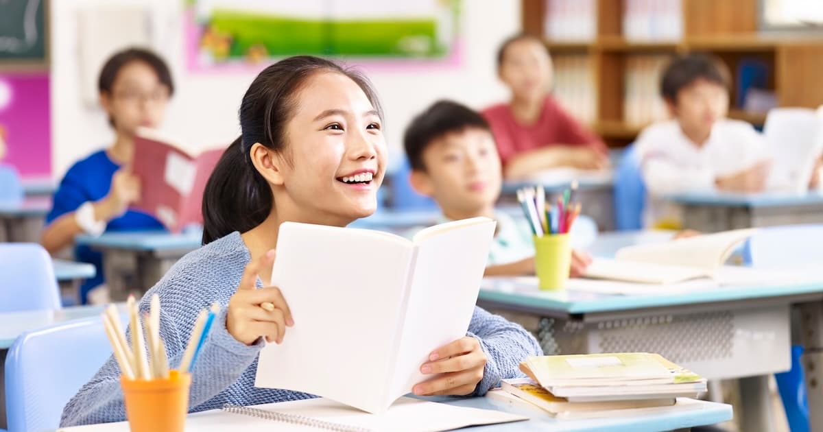 Children engaged in a group activity in a bright classroom with a teacher observing and smiling.