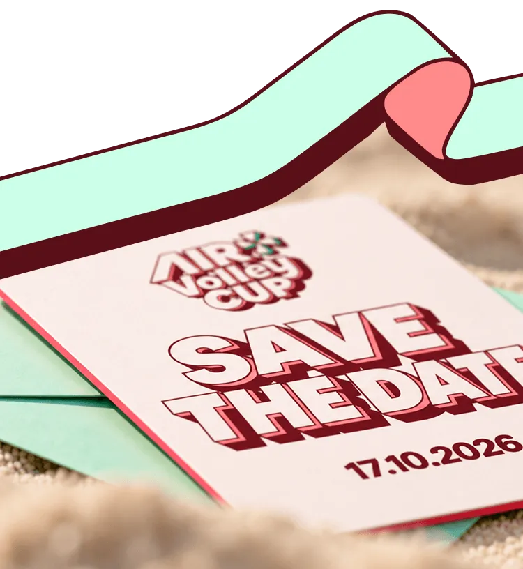 Close-up of a save the date card for the Air Volleyball Cup with the date 17.10.2026 placed on a green envelope on a sandy surface.