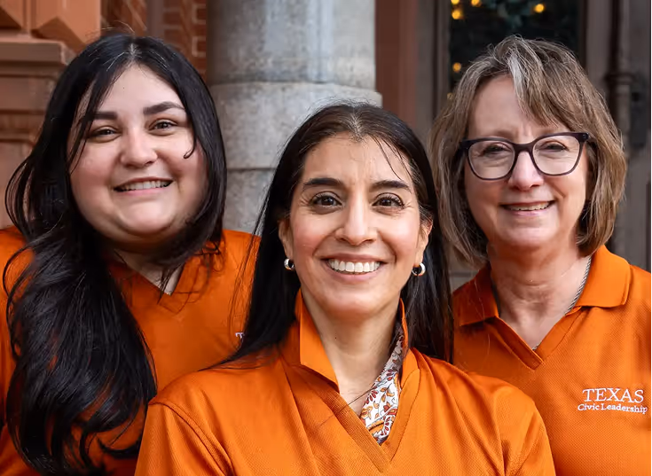 Three women smiling, wearing orange Texas Civic Leadership polo shirts, standing outdoors.