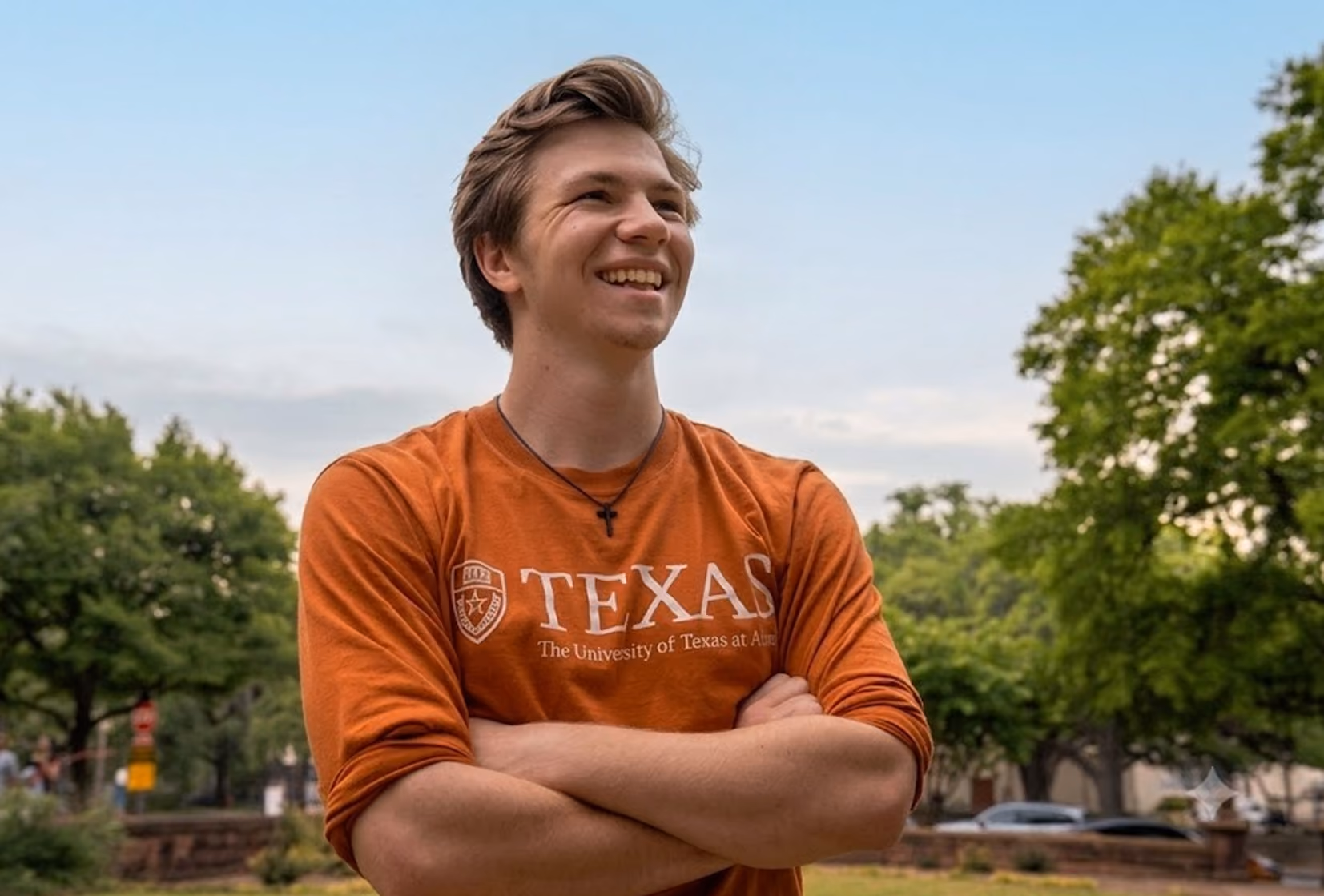 Young man in a Texas University orange shirt smiling outdoors with arms crossed.