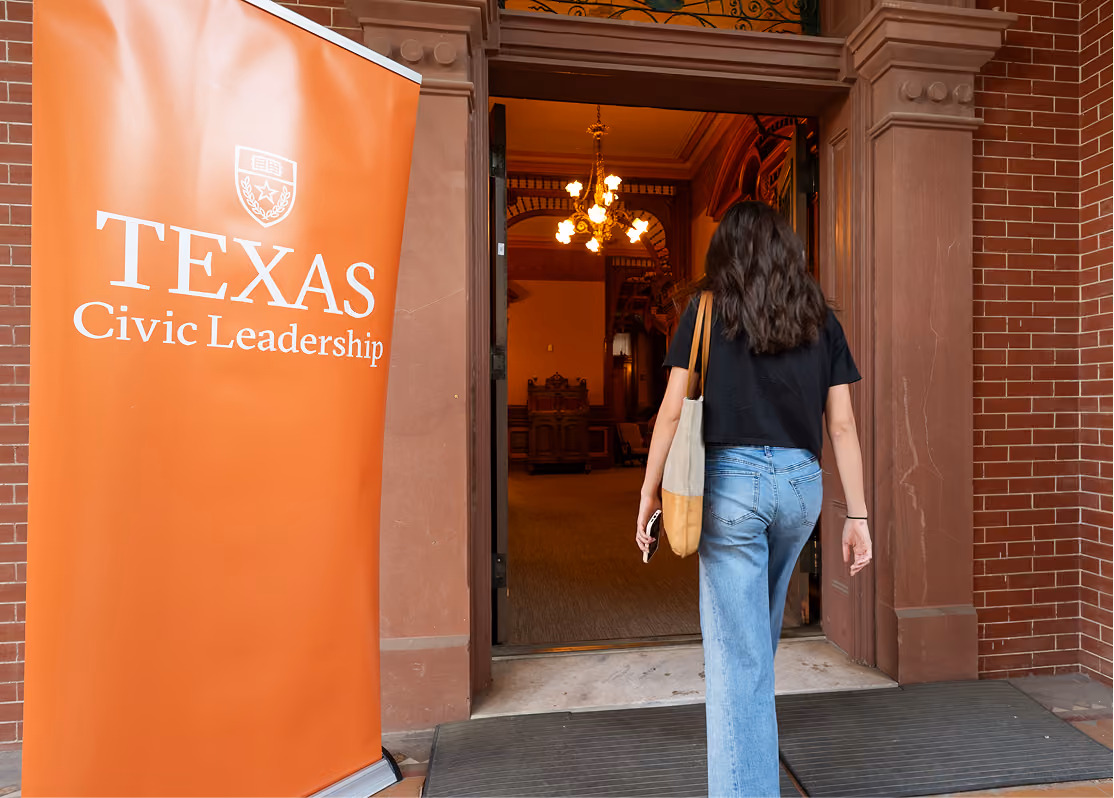 Woman with long hair enters a building next to an orange banner reading Texas Civic Leadership.