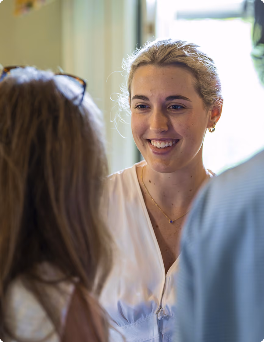 Smiling woman with blonde hair talking to two people indoors in natural light.