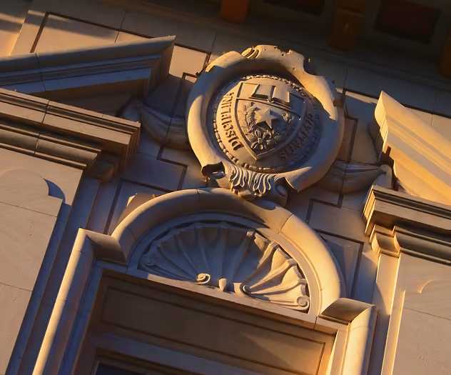 Stone architectural facade with a circular emblem featuring a star and inscriptions above a decorative arched window.