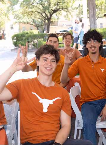 Four young men wearing burnt orange shirts with a longhorn logo making the Hook 'em Horns hand sign.