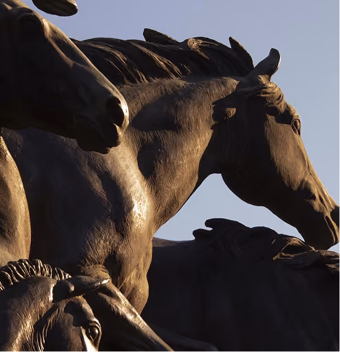 Close-up of dark bronze horse statues against a clear blue sky.