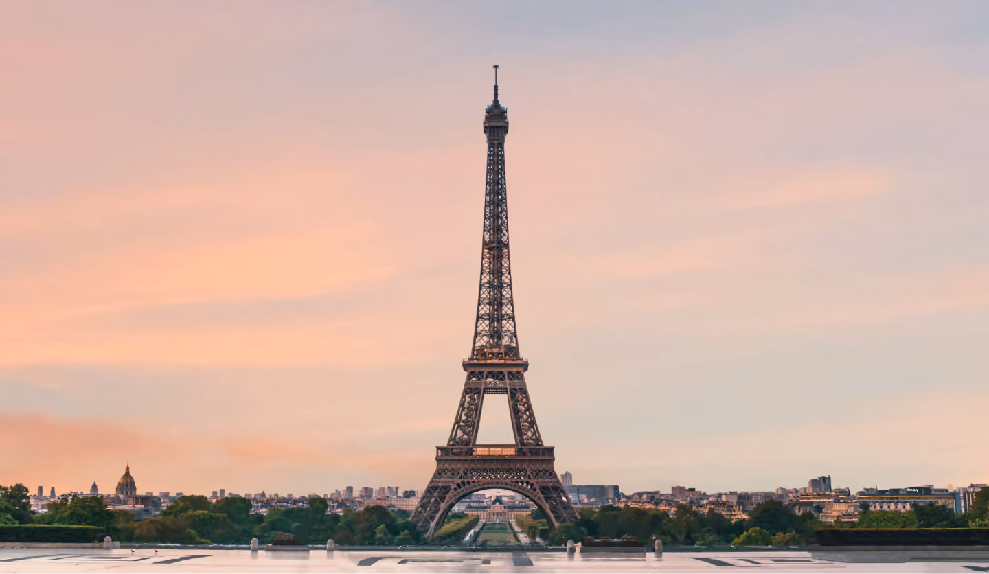 Eiffel Tower centered in Paris skyline during a calm sunset with a pastel pink sky.