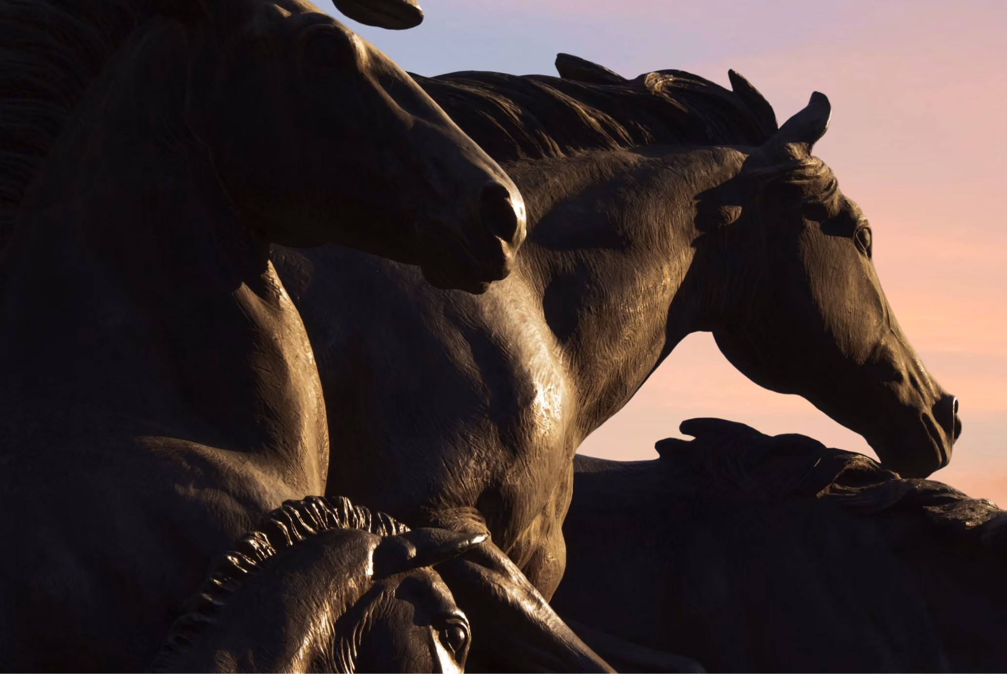 Close-up of dark horse statues with detailed manes against a sunset sky.