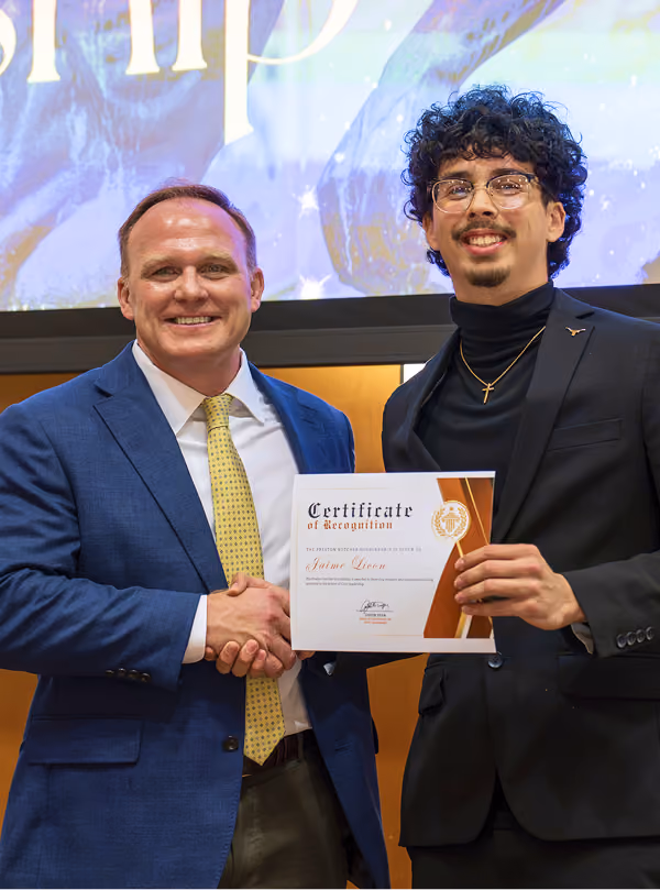 Two men smiling and shaking hands; one holds a certificate of recognition.