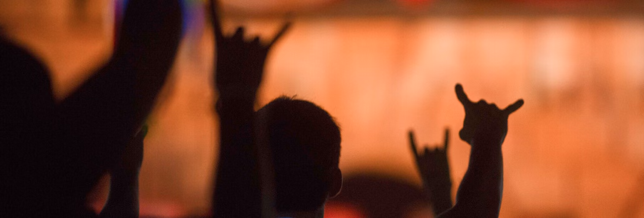 Shadows of people raising hands making rock and shaka signs against an orange background.