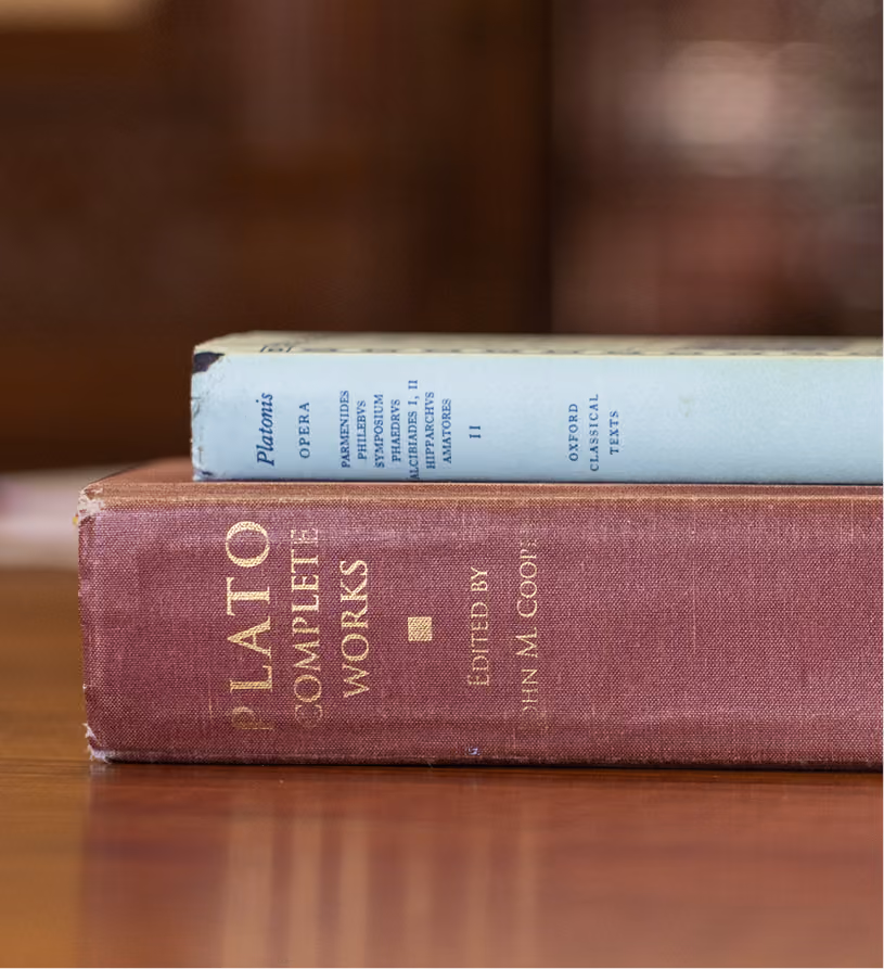 Two hardcover books stacked on a wooden table, one titled Plato Complete Works.