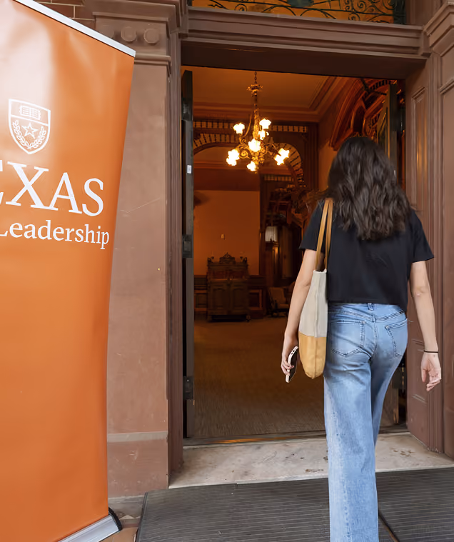 Person with tote bag walking into building entrance near a Texas Leadership banner.