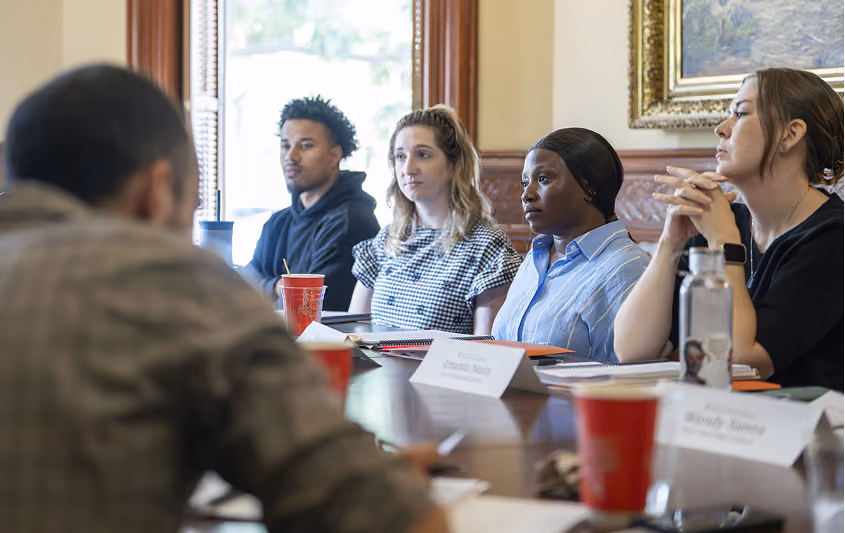 A diverse group of adults attentively listening during a meeting or seminar in a room with wood decor.