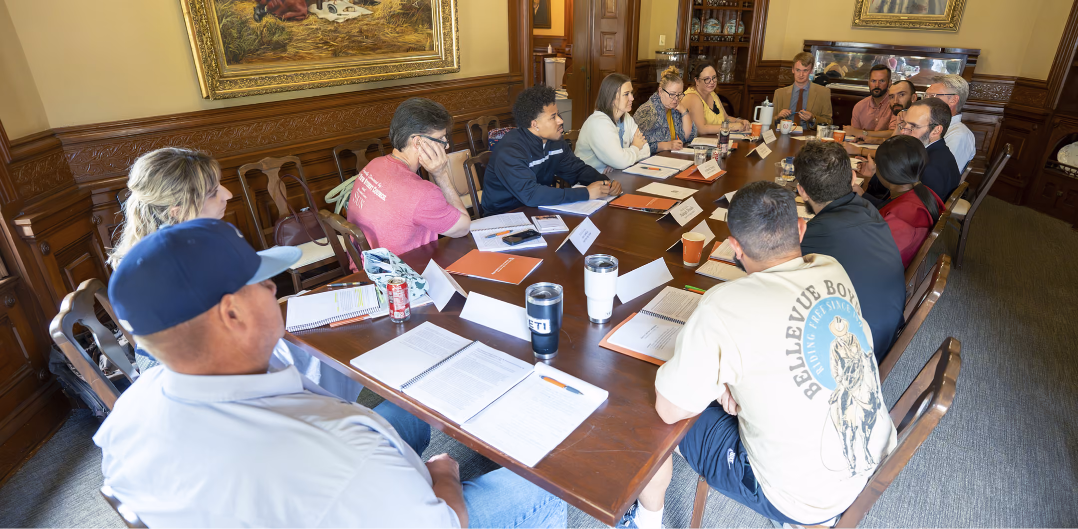 Group of adults seated around a large wooden table in a meeting room discussing documents.