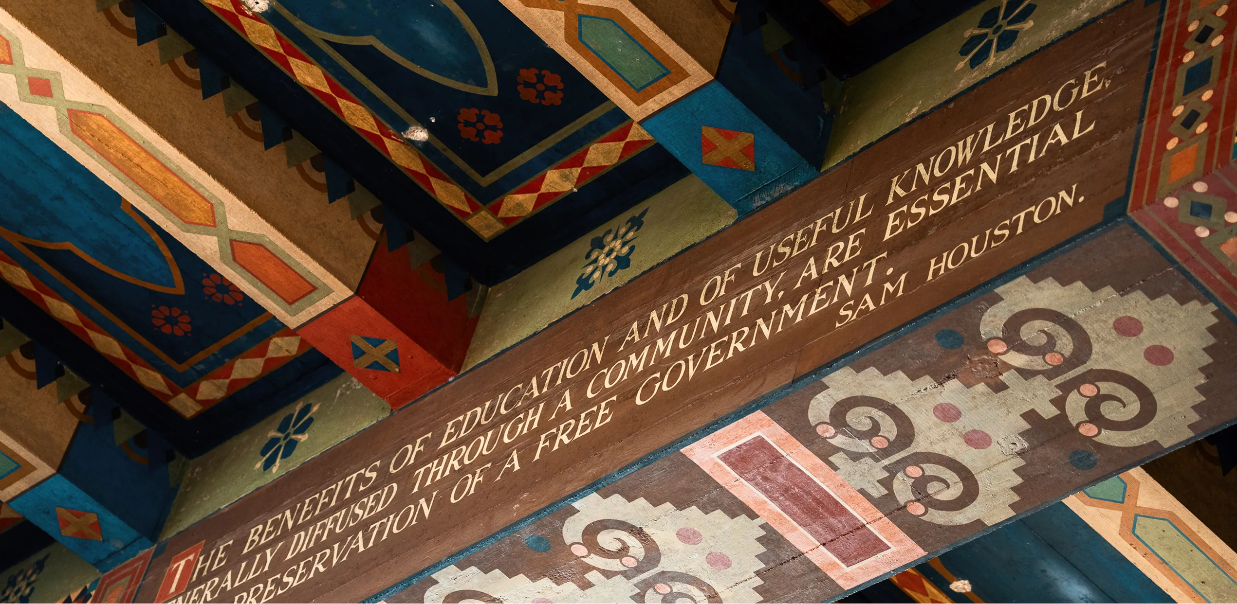 Colorful painted ceiling beams with quote by Sam Houston about education and free government.