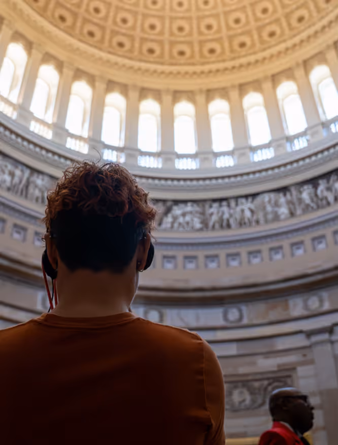 Person wearing headphones viewing the dome interior of a historic building with tall arched windows.