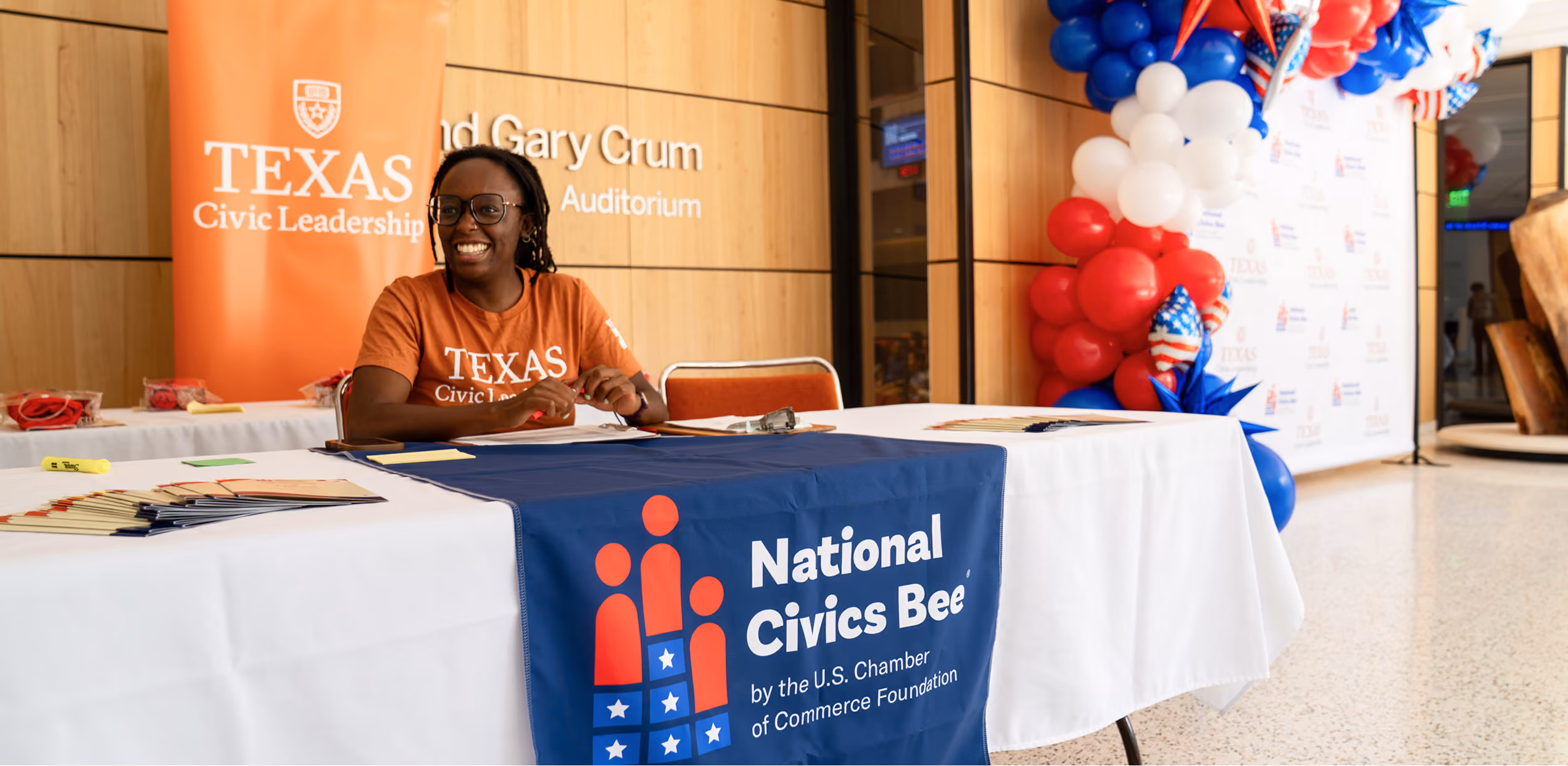 Smiling woman in Texas Civic Leadership shirt at National Civics Bee event registration table.