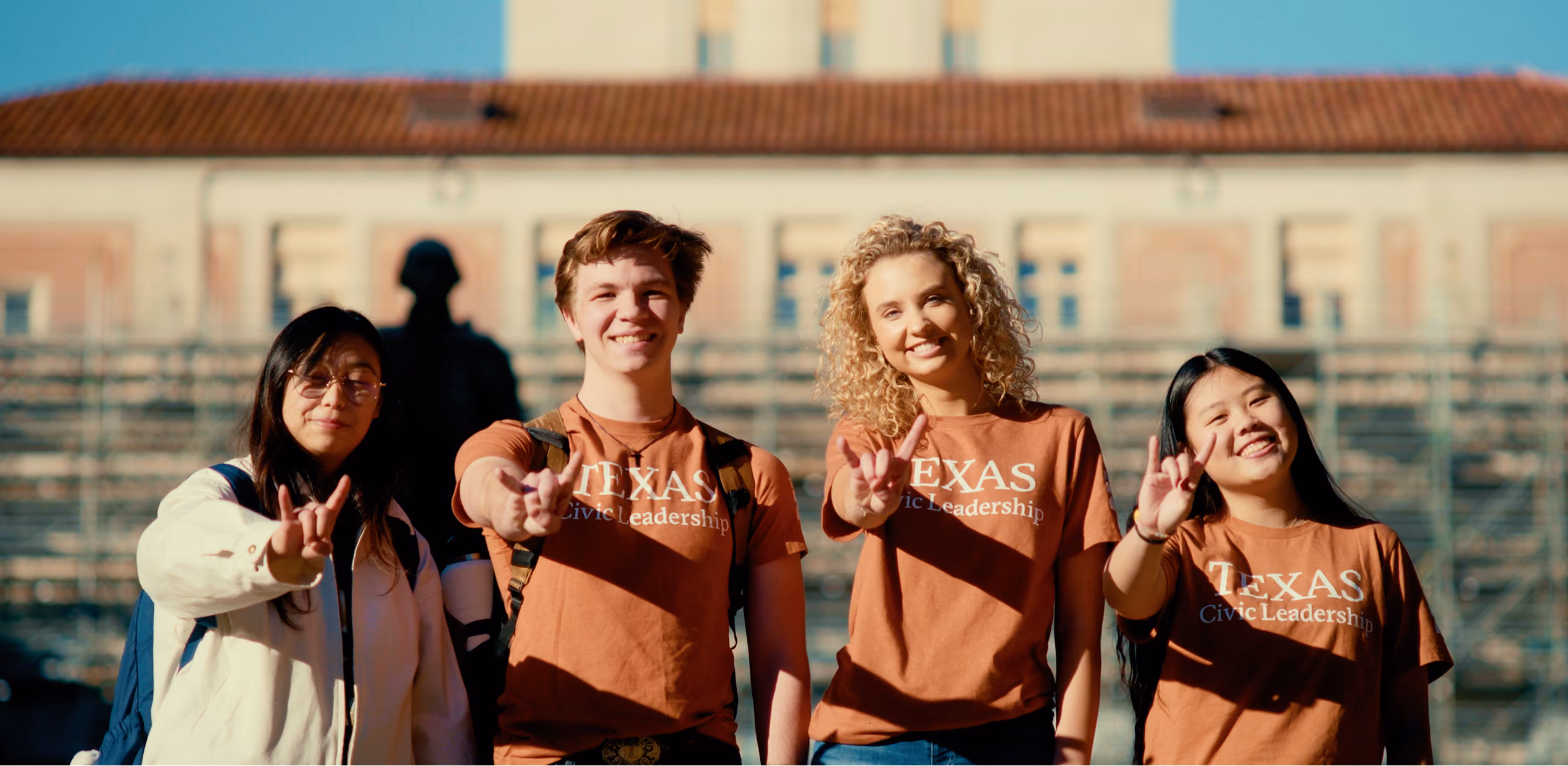 Four smiling students, three wearing Texas Civic Leadership shirts, flashing the Texas hand sign.