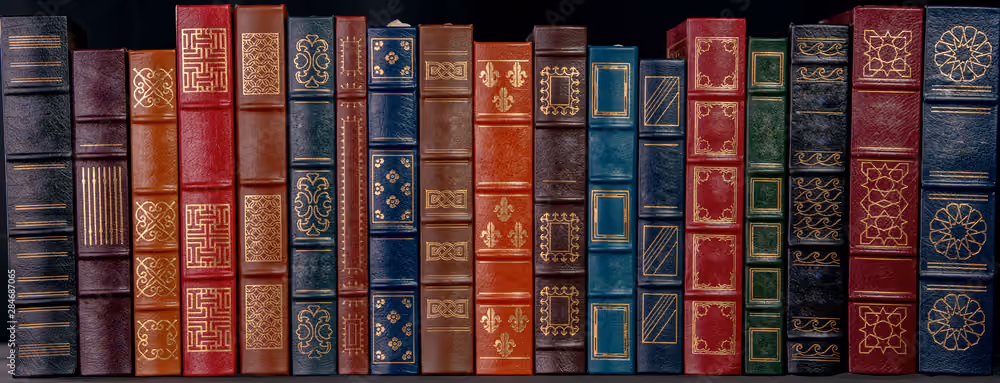 Row of vintage leather-bound books in various colors with gold decorative patterns on spines.