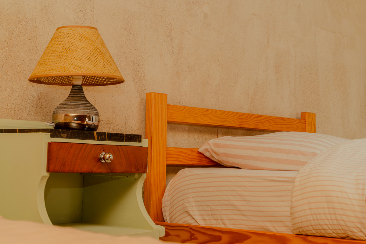 Wooden bed with striped bedding next to a bedside table holding a decorative table lamp.