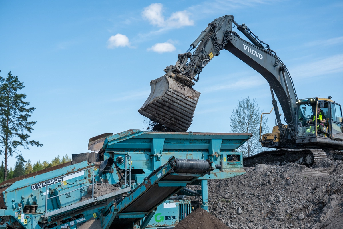Gärvmaskin gräver bland massor och transporterar materialet till sorteringsmaskin.