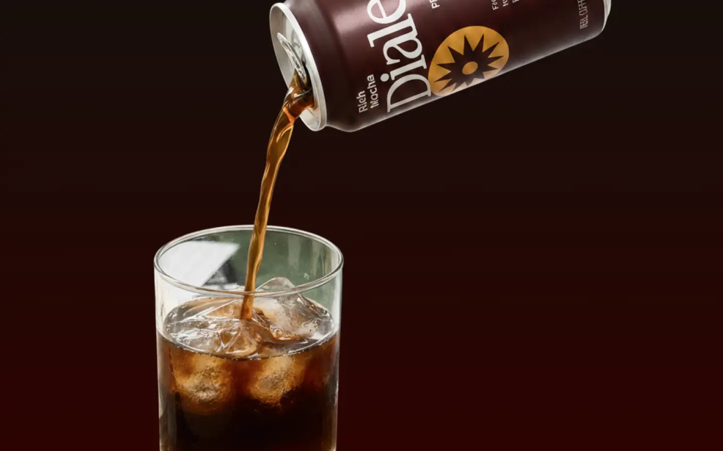 Rich Mocha Dialed coffee being poured from a can into a glass with ice cubes.