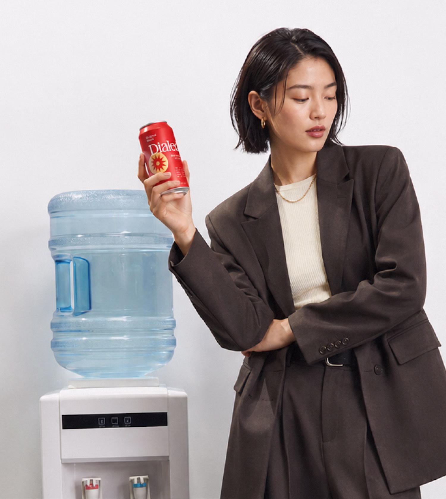 Woman in a dark suit holding a red can labeled Dialed next to a white water cooler.