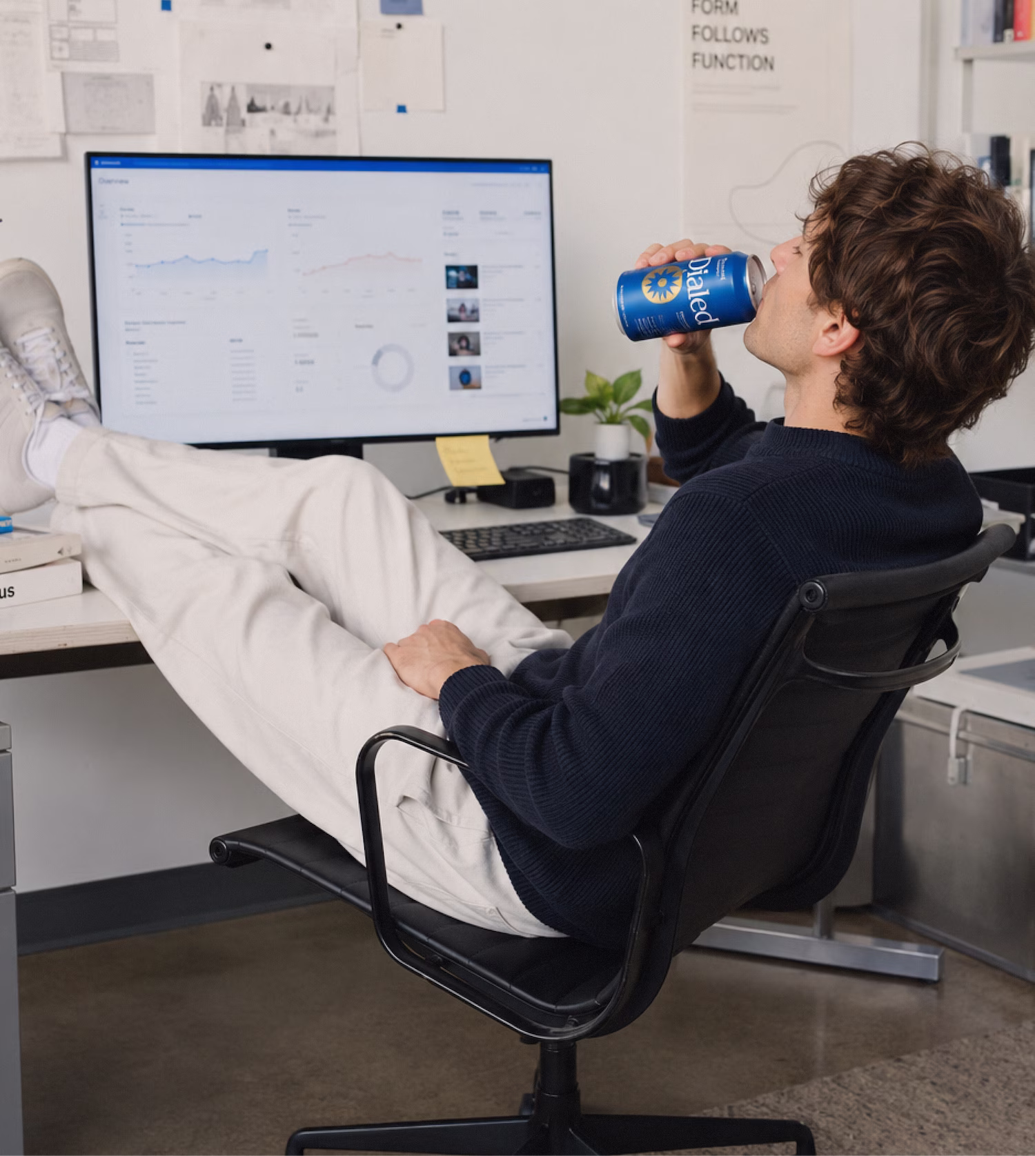 Man sitting in office chair with feet on desk drinking from a blue Dialed soda can.