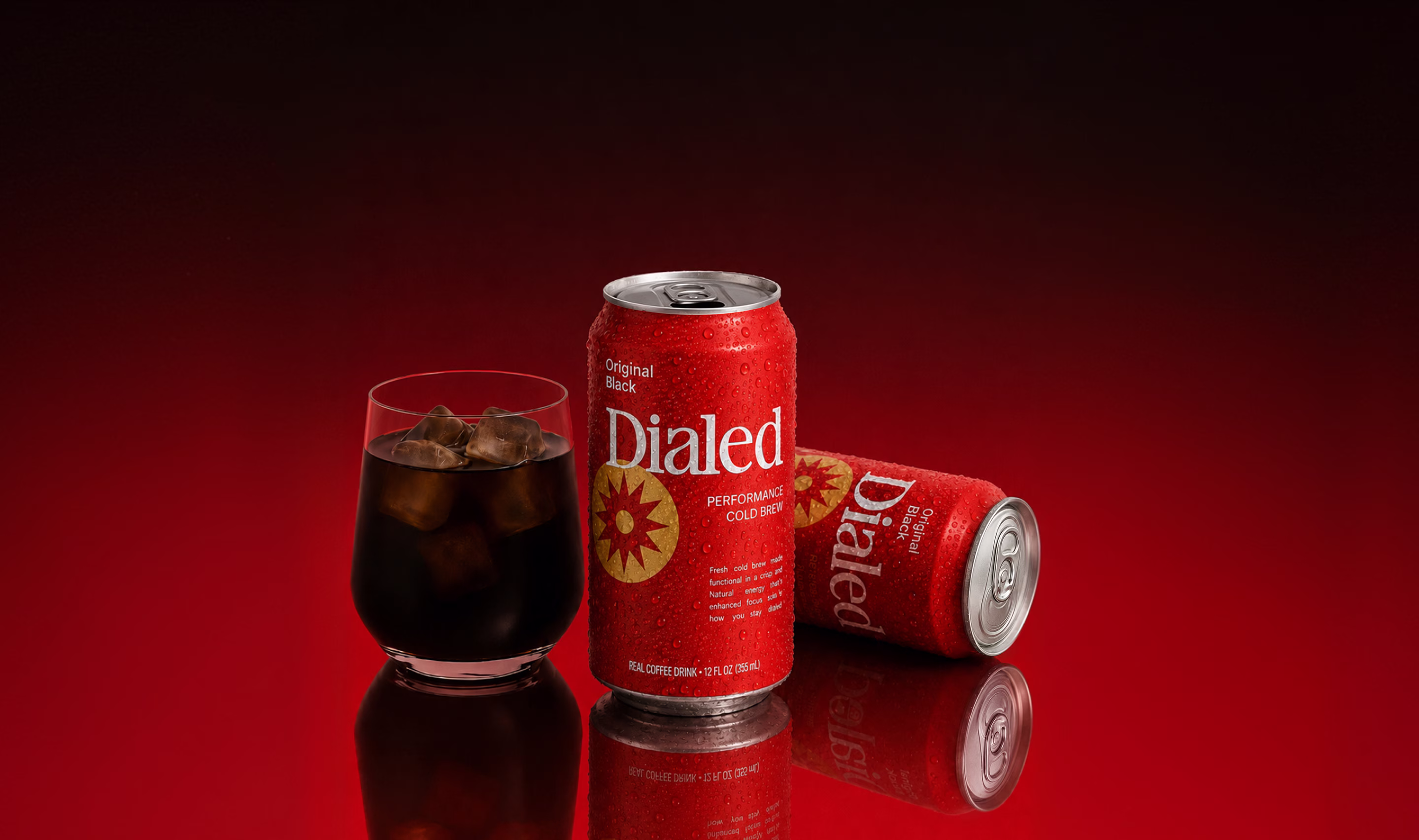 Two red cans of Dialed cold brew coffee with a glass of iced coffee on a red reflective surface.
