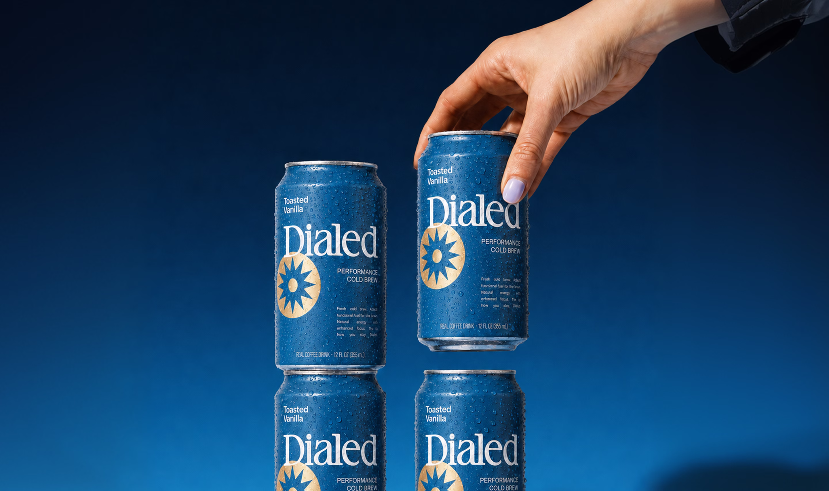 Four blue cans of Dialed Toasted Vanilla cold brew stacked with a hand reaching for the top right can.