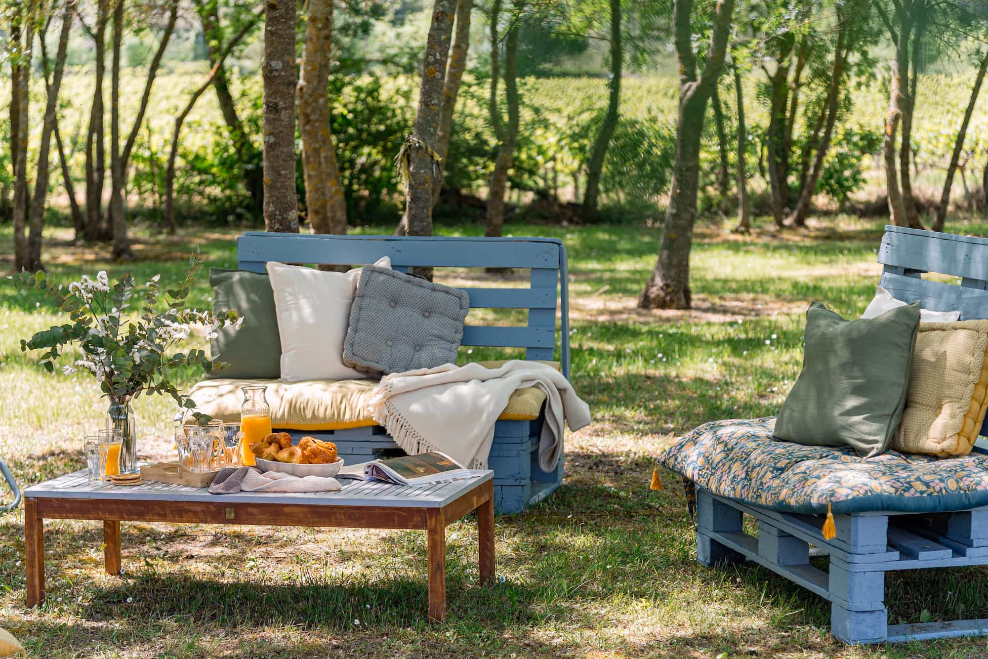 Deux canapés en palette bleue avec coussins et table basse en bois sur pelouse ensoleillée.