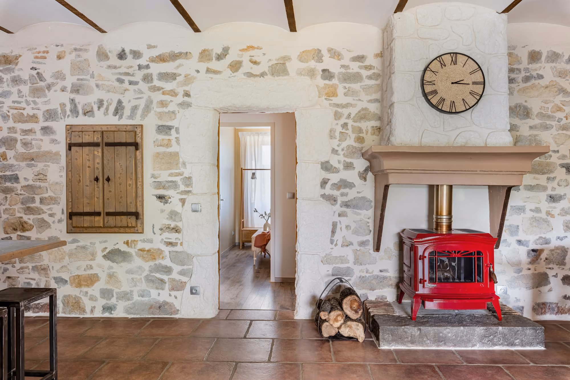 Salon avec poêle à bois rouge sur un socle en pierre et un mur en pierres apparentes.