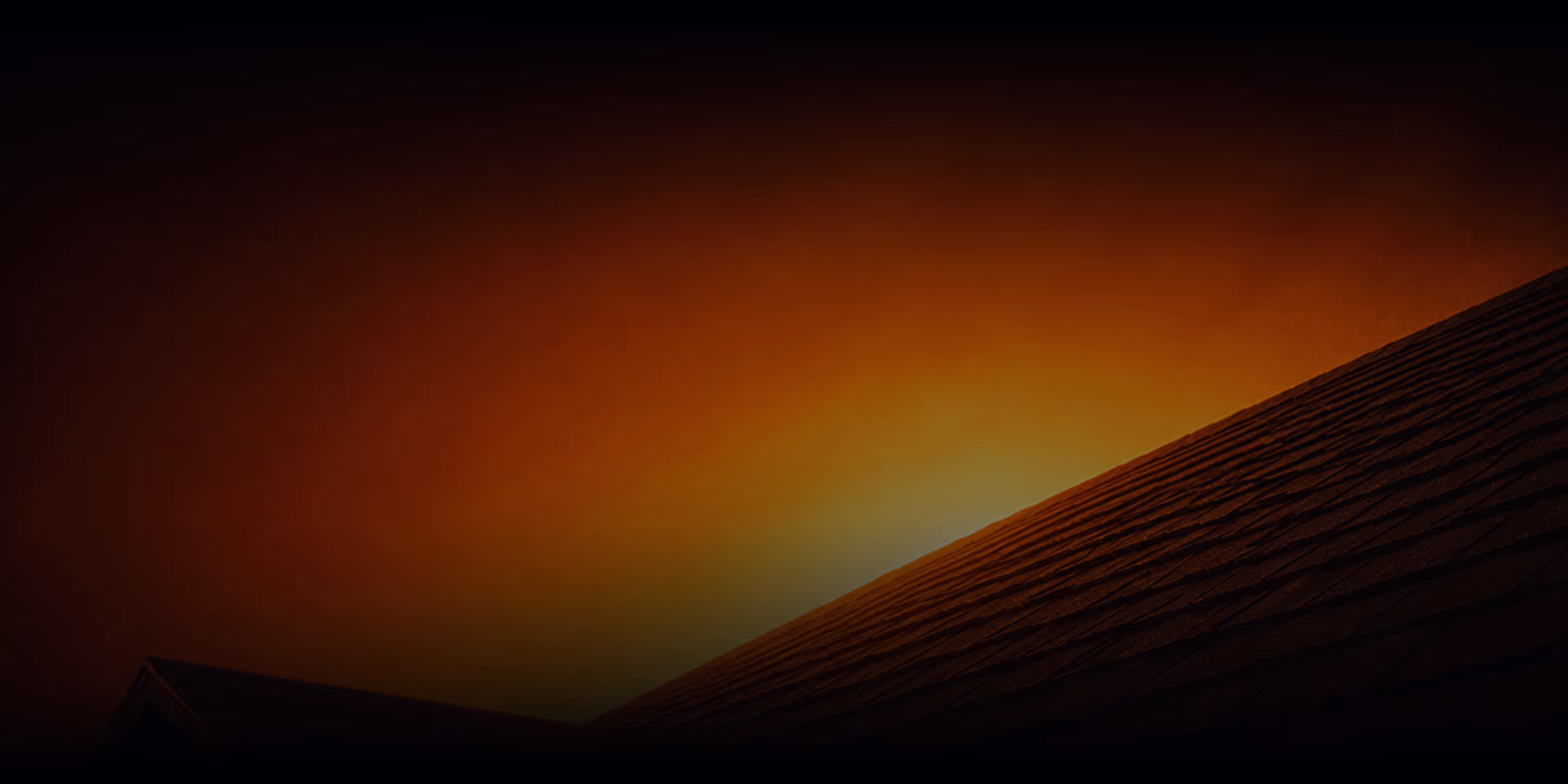 Silhouetted rooftop against a vivid orange and yellow sky at sunset or sunrise.