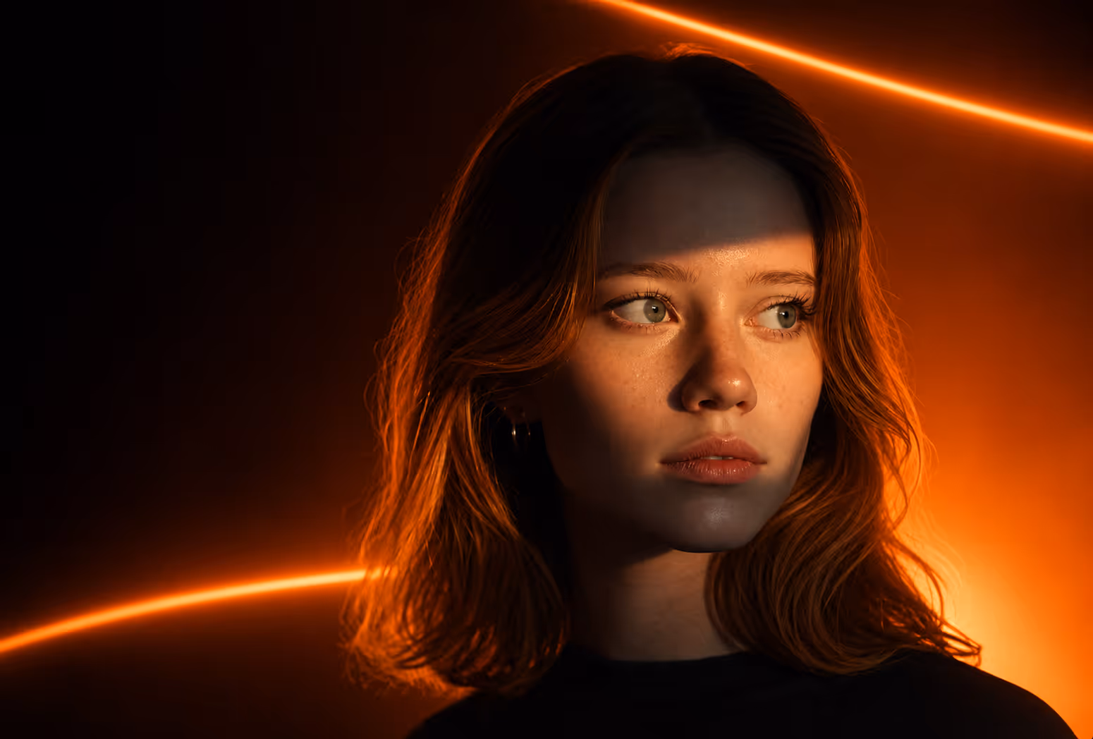 Young woman with wavy hair lit by orange neon light lines against a dark background looking right.