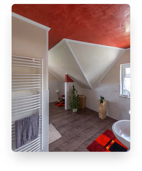 Badezimmer mit roter Decke, geneigtem Dach, Pflanzen, Handtuchheizung und buntem Teppich.