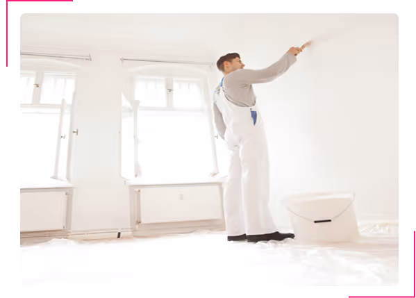 Mann in weißer Arbeitskleidung streicht mit Pinsel eine weiße Wand in hellem Raum.