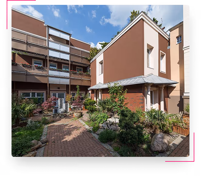 Innenhof mit Backsteinweg, verschiedenen Pflanzen und modernen Wohngebäuden bei Tageslicht.