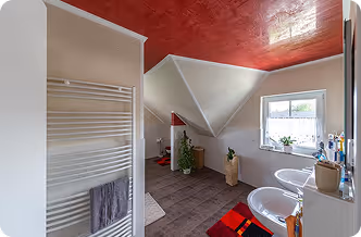 Helles Badezimmer mit roten Decken, zwei Waschbecken und Dachschräge mit Fenster.