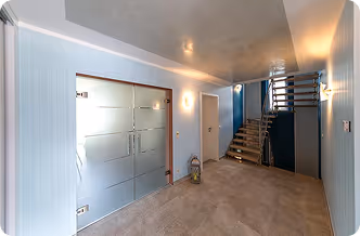Heller Flur mit moderner Glastür, Treppe und blauen Wänden in einer Wohnung.